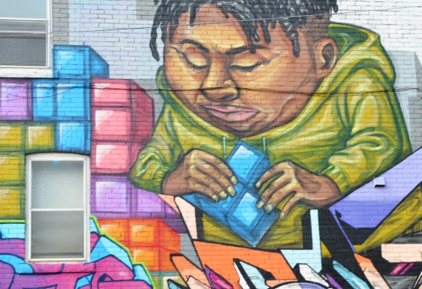 part of a mural by elicser of a couple putting tetris shapes together on a wall - heavy man in a long sleeved green hoodie