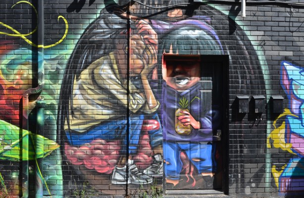 elicser mural on Croft street, man in doorway with a drink in a pineapple in his hand, other person sitting with hand over face 