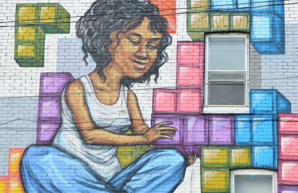 part of a mural by elicser of a couple putting tetris shapes together on a wall - woman in blue jeans and white sleeveless top