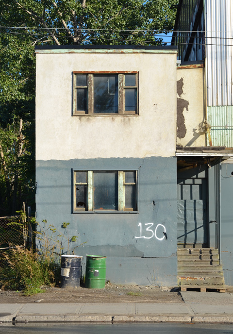 part of an empty and abandoned building, two storeys, old windows, the number 130 written in large white numbers 