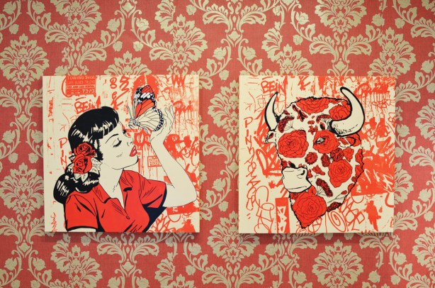 two pictures on a gallery wall, in red, black and white, on wallpaper that is red and beige intricate floral pattern 