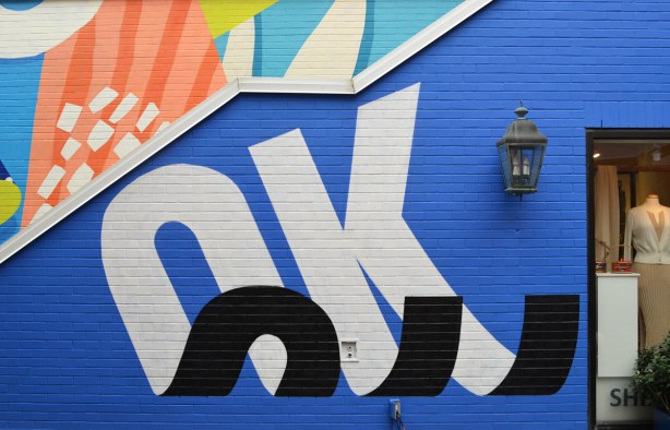 on the side of outdoor steps, a blue mural with the word OK in black and white such that it looks like the letters are curling up at the ends, 3 D effect 