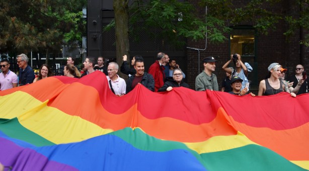 people holding the edge of a large pride rainbow flag 