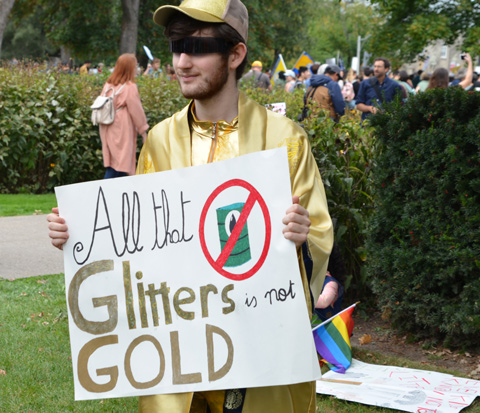 at the climate strike rally at Queens Park on a sunny morning in September, a young man dressed in gold and holding a sign that says All that glitters is not gold 