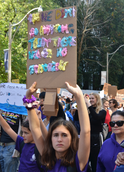 people at Toronto climate strike, walking along Wellesley street with signs, a cardboard sign with tissue paper glued on for the letters, difficult to read