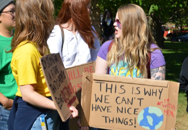 at the climate strike rally at Queens Park on a sunny morning in September, group of young people, including a woman with a cardboard sign that says This is why we can't have nice things