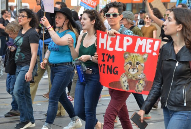 people at Toronto climate strike, walking along Wellesley street with signs, person in sunglasses carrying red sign that says help me I'm dying with a large picture of a baby leopard 