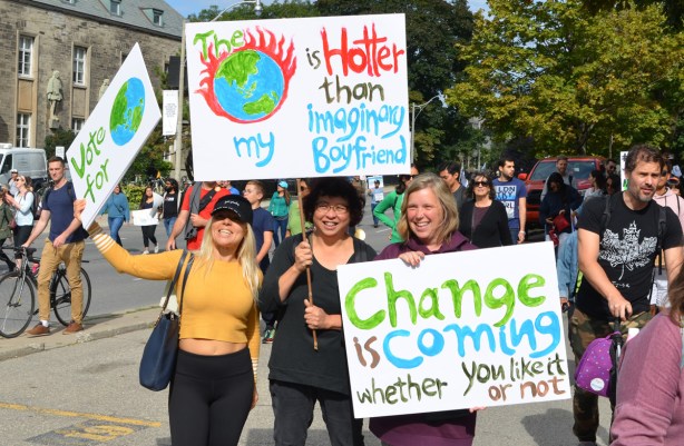 three people holding three placards, one says The earth is hotter than my imaginary boyfriend. also one says Change is coming whether you like it or not.