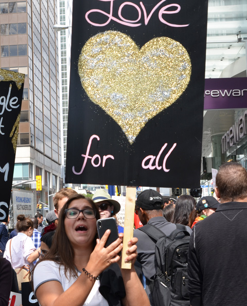 a young woman holds up a black sign with a large gold heart on it and the words love for all