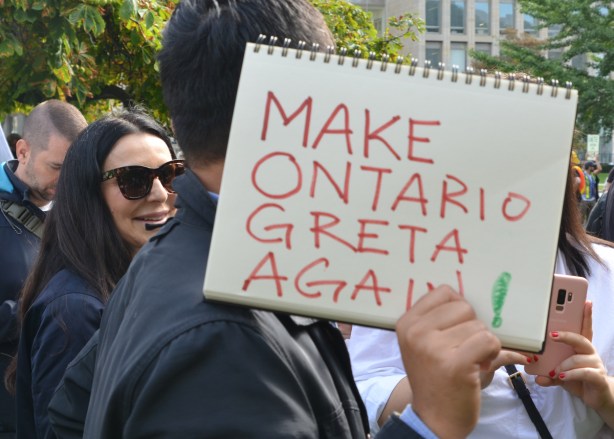 a man holds a spiral bound sketch book on which he's written Make Ontario Greta again.