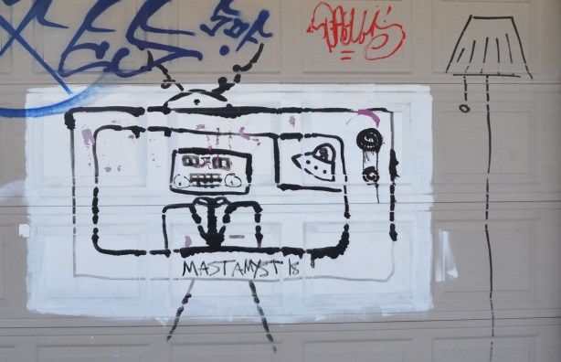 on a beige garage door, a white rectangle painted and on that, black drawing of a man with with a square head on TV, a lamp is beside the television 