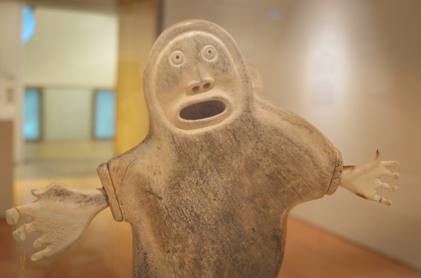 whale bone sculpture in art gallery, mother and child, large round face with open mouth and two outstretched arms with large hands