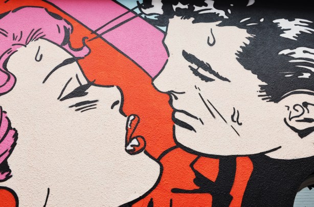 close up of a mural, a man and a woman are leaning together for a kiss. Woman has bright red lipstick. 