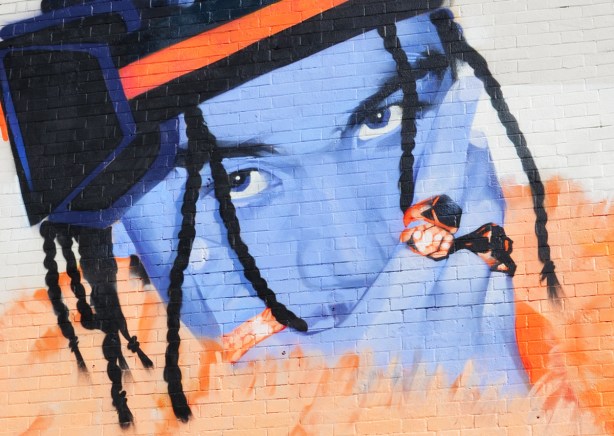 close up of part of mural, blue face, orange furry scarf, person wearing two rings, hat, dreadlocks, 