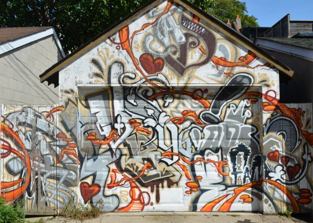 older mural on garage and fence on both sides, covers the whole thing, in oranges, browns, and greys, 