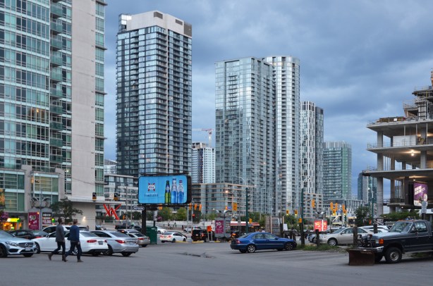 looking across parking lot at north east corner of Spadina and Front towards the traffic and lights at the intersection, billboard, people 