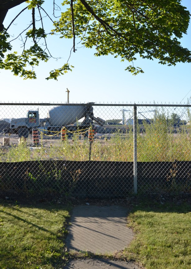 a path leads to a fence, construction site behind the fence, including a cement truck 