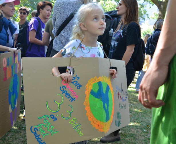 a young girl holds a carboard sign that has a picture of of a peace sign made with a picture of the Earth 