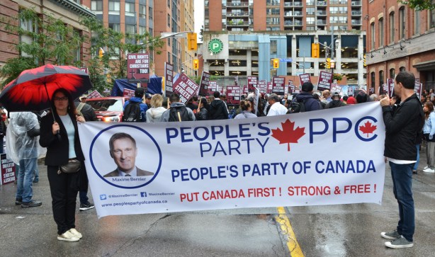 large white banner for the Peoples Party of Canada, in front of a protest on Church street 