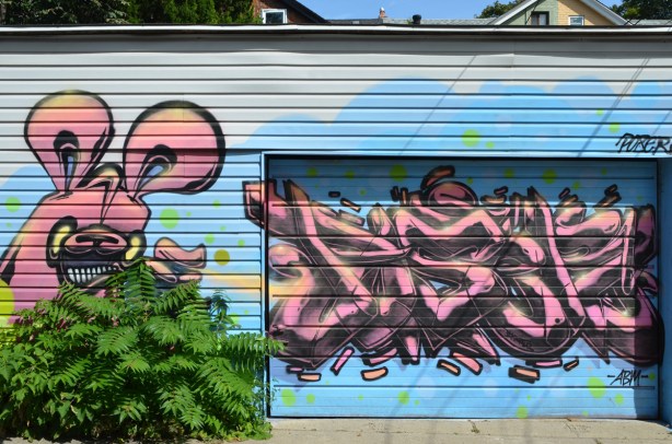 poser bunny and text, pink bunny, pink text, on light blue background, text is on garage door, bunny is on wall beside door 