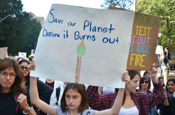 people at Toronto climate strike, walking along Wellesley street with signs, girl holds sign that says save our planet before it burns out