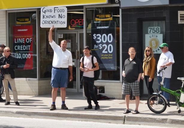 a man across the street from a protest holds up a sign that sign that says good food knows no orientation