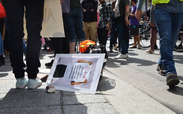 a protest sign lies on the sidewalk as people pass by 