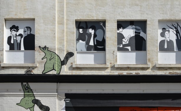 black and white pictures in the windows, green raccoons on the walls, looking at one of the pictures 