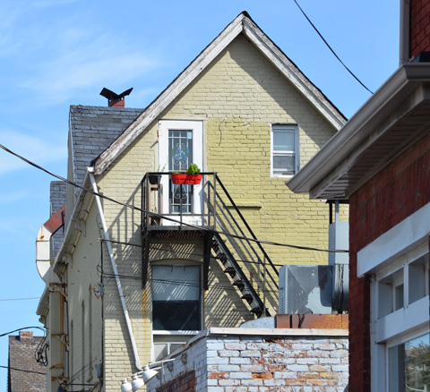 upper storey door with metal stair case and its shadows. White door. Red flower box on railing outside door. 