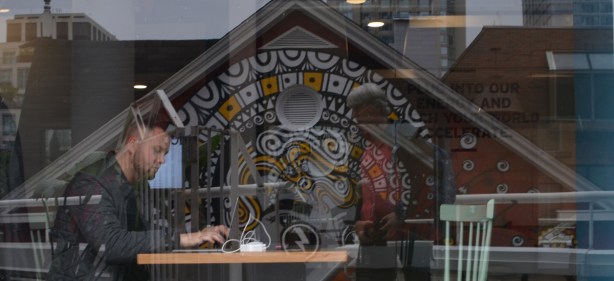 man working at a table, with reflections of a mural in the window, looking through the window 