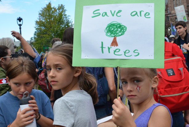 at the climate strike rally at Queens Park on a sunny morning in September, a young girl holds a homemade sign that says save are trees, two other girls are with her