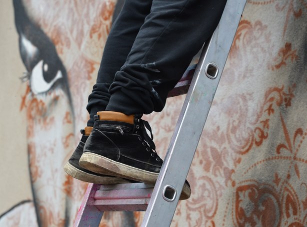 shoes on a ladder with the eye of a mural looking at them 