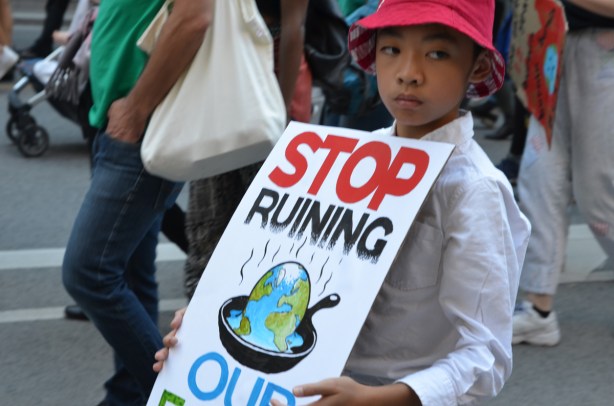 young boy with sign that says Stop ruining our planet 
