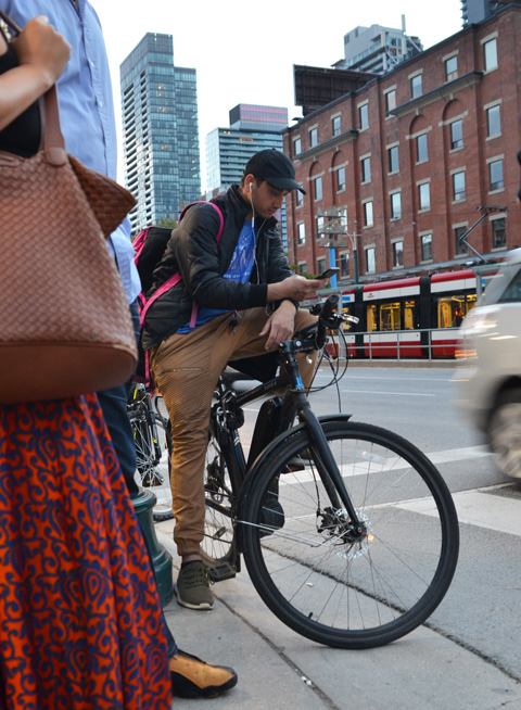 a young man sits on his bike and checks his phone while waiting at an intersection for the traffic lights to change