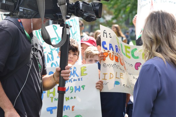 at the climate strike rally at Queens Park on a sunny morning in September, a group of school kids holding protest signs that they've made, but keeping their eyes on a man with a large TV camera
