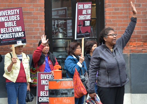 a group of wimen lined up against a wall, on the street, with hands in the air, some have signs that say Civil rights are for Christians too 