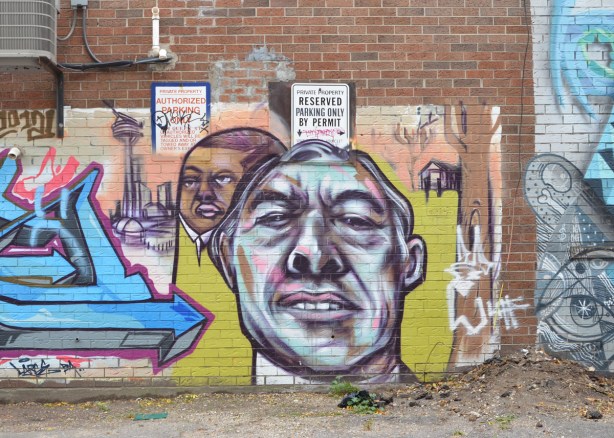 older mural by elicser of two men, one head is much larger than the one behind it