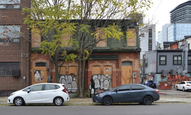 an old brick two storey semi detached house with green mansard roof is boarded up and empty