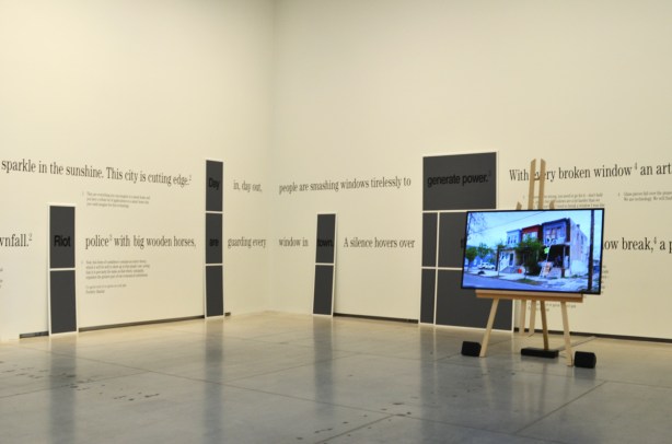 room at the Art Gallery of Ontario with words written around the walls, and a flat screen TV laying a video in the middle of the room