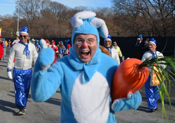 a man dressed as a blue and white rabbit hamming it up for the camera. He's carrying a large stuffed carrot shaped object 