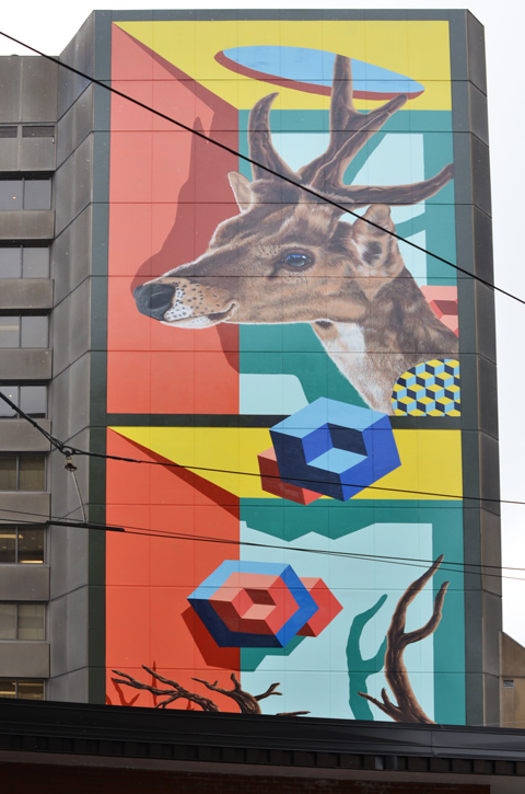 large mural by birdo, vertical, on the side of a building, with a realistic deer head at the top