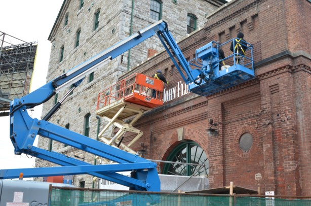 men on a blue lift crane at the distillery district, old brick building