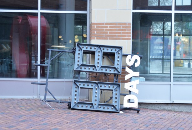 leaning against the side of a building, on its side on the ground, the sign at the distillery district that says how many days left until Christmas
