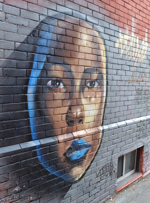 a large woman's face painted on the side of a brick building 