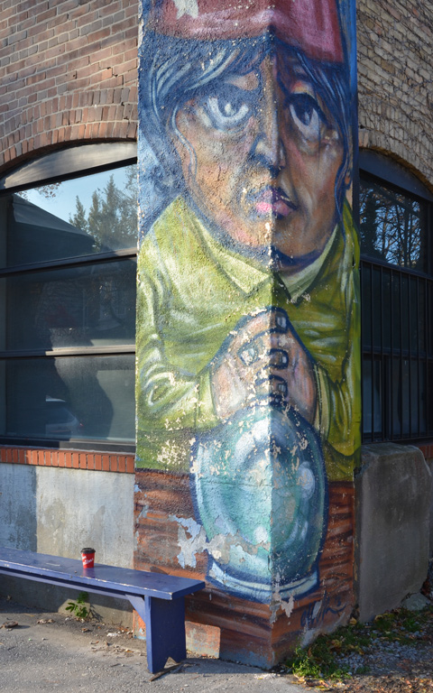 a painting of a man with hands folded in front, and wizard cap on, on the exterior corner of a building 
