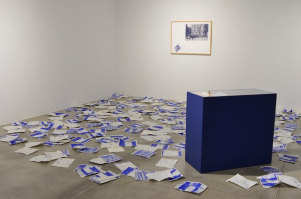 blue and white papers strewn over the floor, discarded, with a framed picture on the wall, and a blue desk in the middle