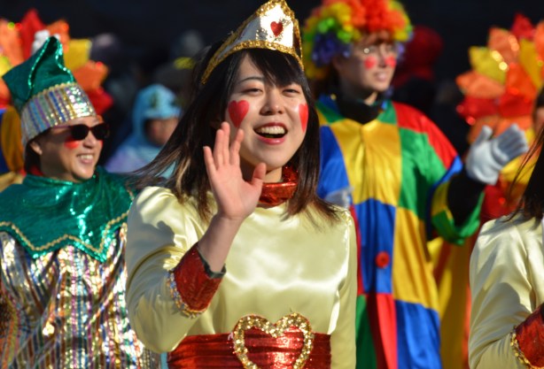 woman in gold costume as Queen of hearts in parade, heart shaped red marks on cheeks, heart on belt and on gold crown, 
