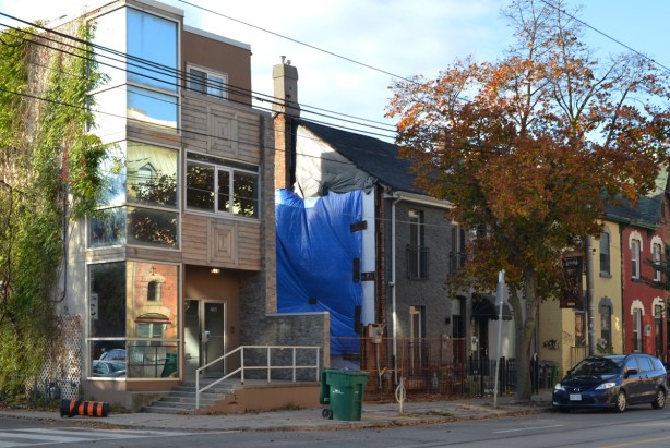a new three storyhouse on the corner, a vacant lot beside it with blue covering as a new home is being built, other houses down the street after that 