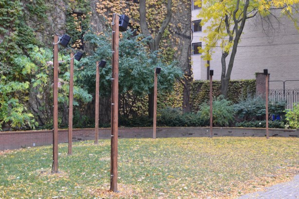in a garden, on flat space, grass, wood poles with small speakers attached to the top of them