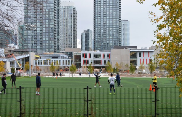men playing soccer on green fake grass playing field in front of Toronto skyline, at Canoe Landing Park